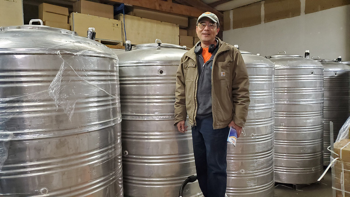 Ray Lam stands next to his custom-made, 300-gallon hot water tanks that can produce 700 gallons of hot water with zero electricity.