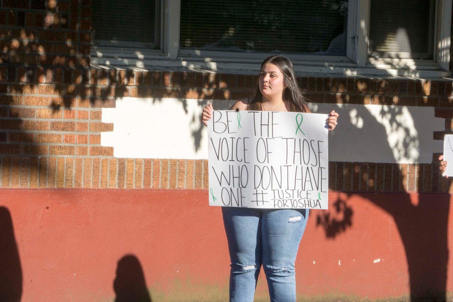 Elena Valencia, the protest’s organizer, stands on the corner of West Maple Street and North Pearl Street holding a sign.