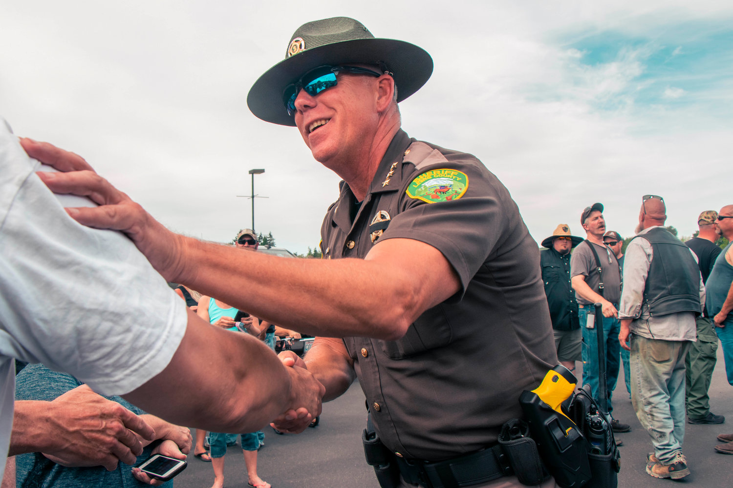 Sheriff Rob Snaza shakes hands with Hamilton sign supporters in the parking lot of Bethel Church Tuesday afternoon in south Chehalis.