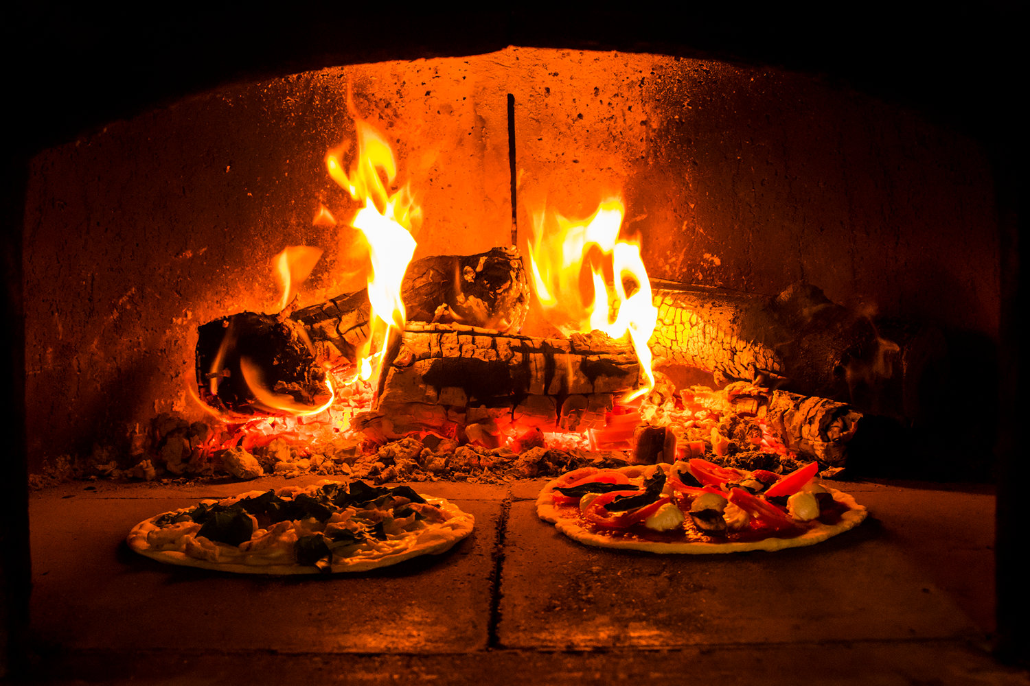 A garlic chicken pizza and a margarita pizza cook inside a wood fire oven inside the Milltown Pizza food cart Tuesday afternoon in Chehalis.