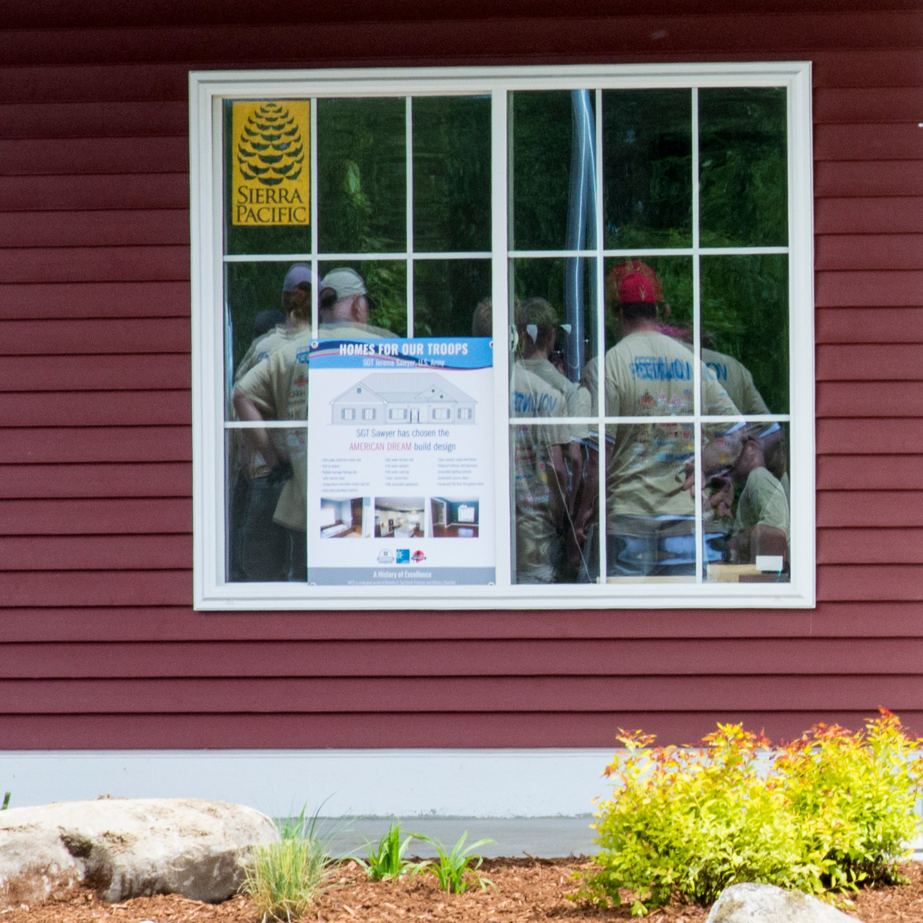 Volunteers are shown in the reflection of a window Saturday morning during an event at the soon-to-be home of wounded veteran Jereme Sawyer.
