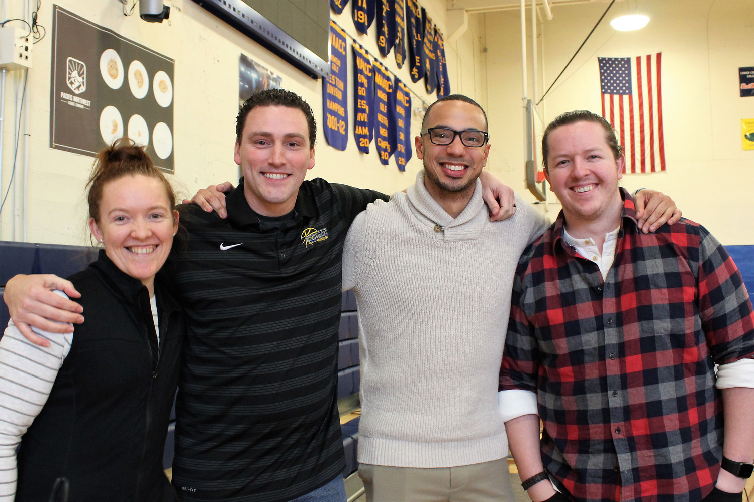 Pacific Northwest Cookie Company owner, Callie Carpenter, Centralia College Men's Basketball head coach, Jason Moir, assistant men's basketball coach Jonathan McMillan and PNW Cookie Company operations Manager, Alex Carpenter, pose in front of the Chehalis company's banner in the Centralia College gymnasium. The company is sponsoring an upcoming cookie giveaway and other sponsorship activities to bolster the amount players will receive to offset their food costs during away games and tournaments.