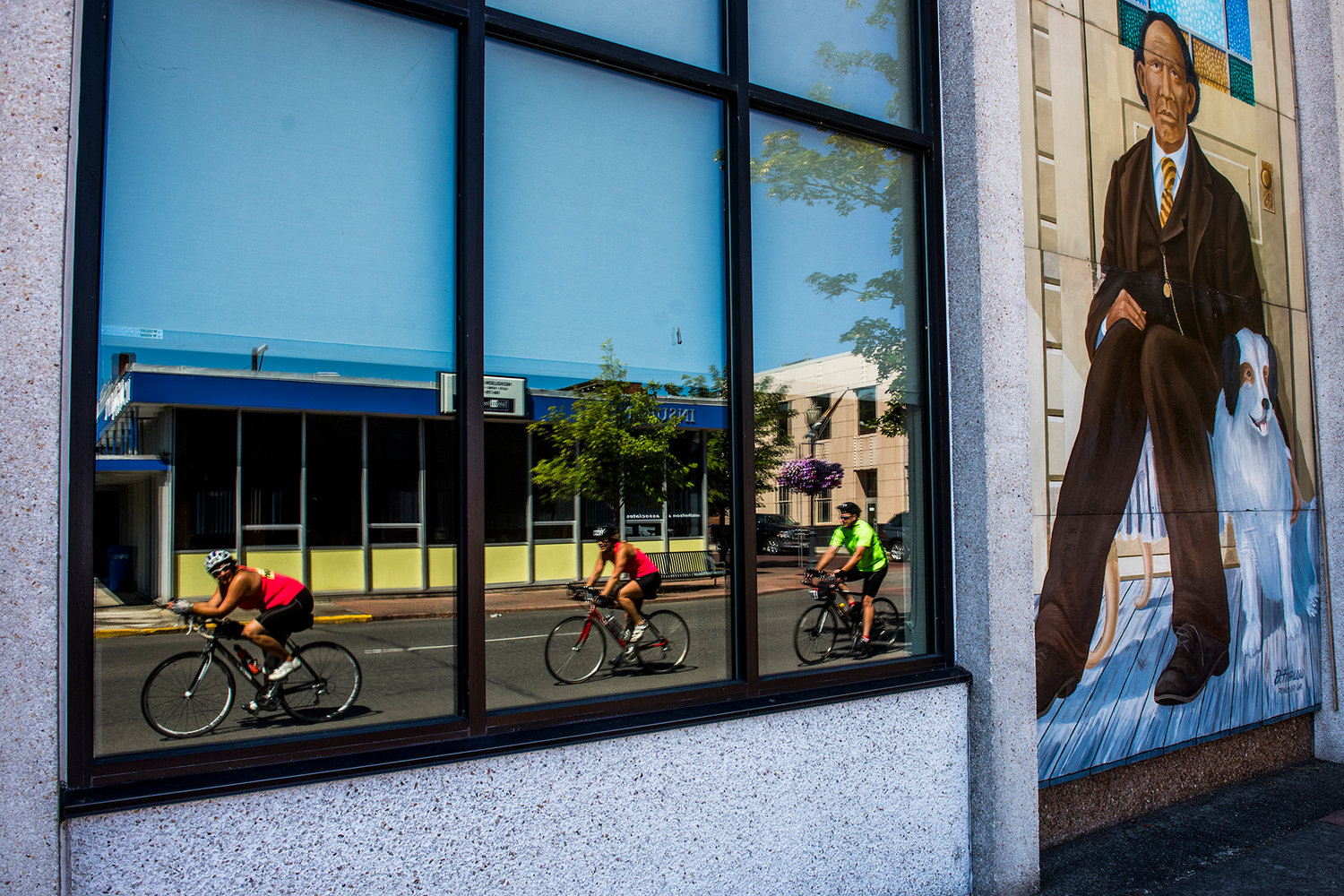 A trio of cyclists make their way along Pearl Street on Saturday afternoon while a mural of George Washington and his trusty dog keep a watchful eye.