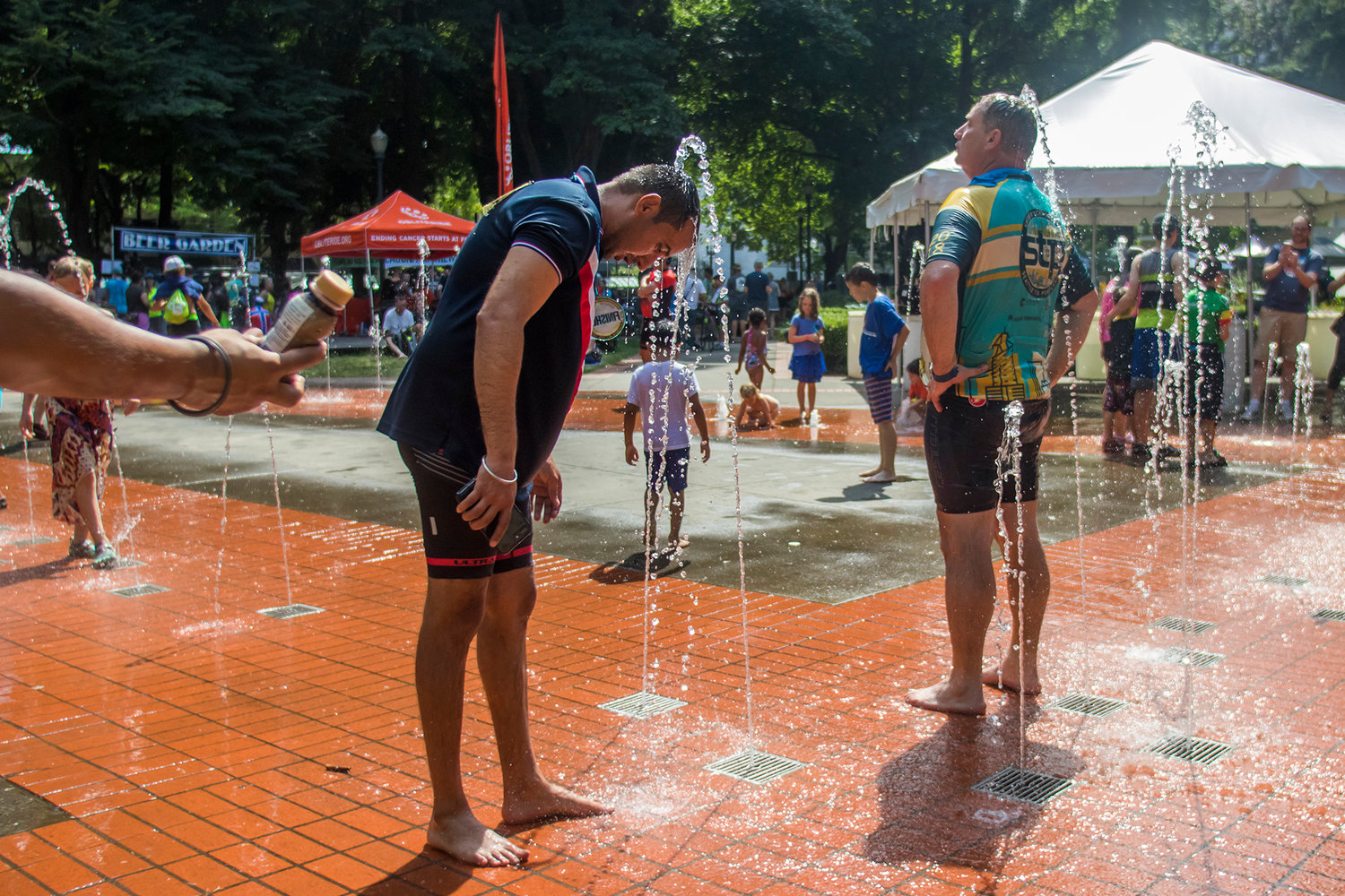 A man holds out a bottle of chocolate mile as STP finishers rinse off in a nearby water park Sunday afternoon at Holladay Park in Portland, Oregon.