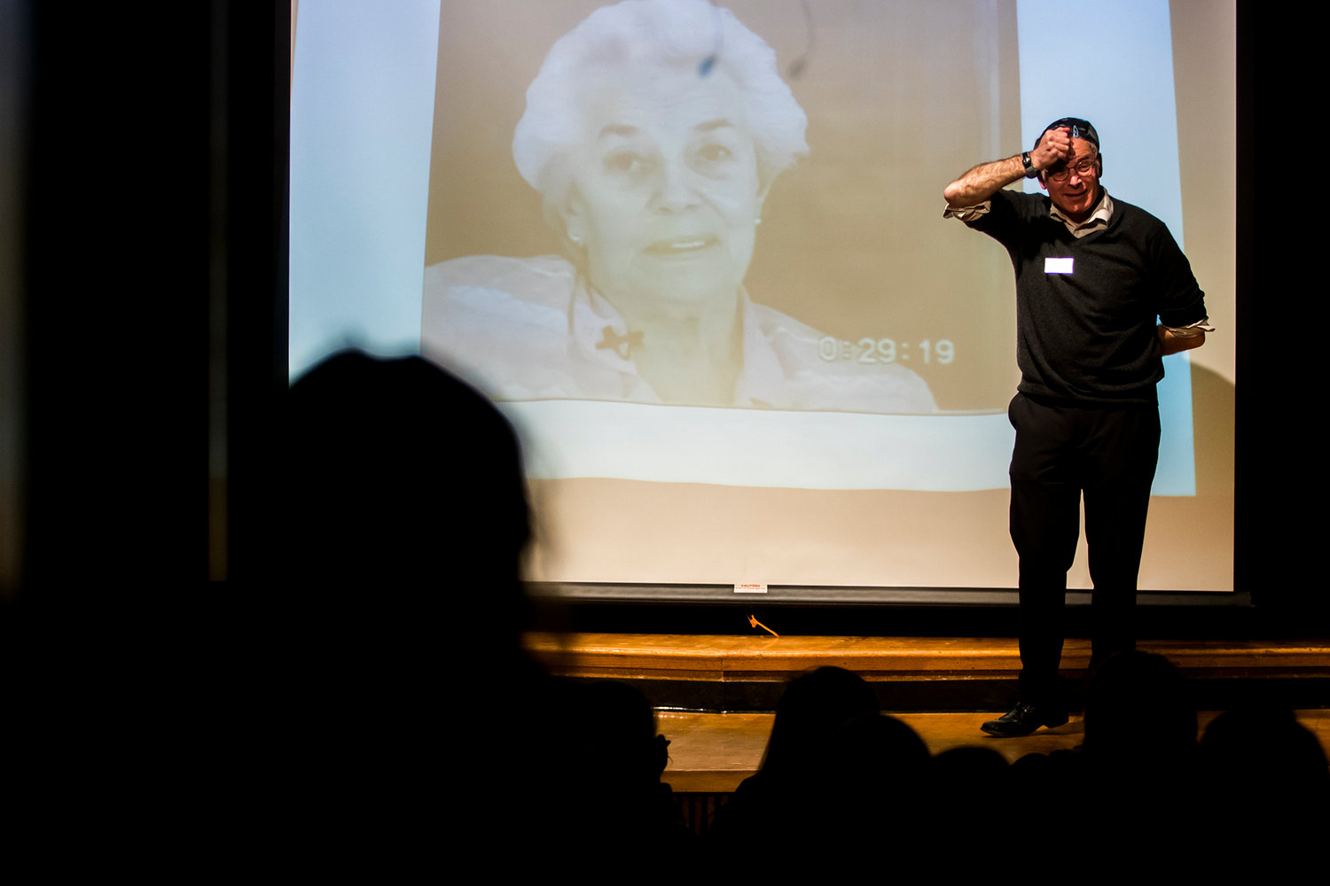 Matthew Erlich stands on stage in front of a picture of his mother Felicia Lewkowicz (born June 21, 1924) who survived two Nazi death camps.