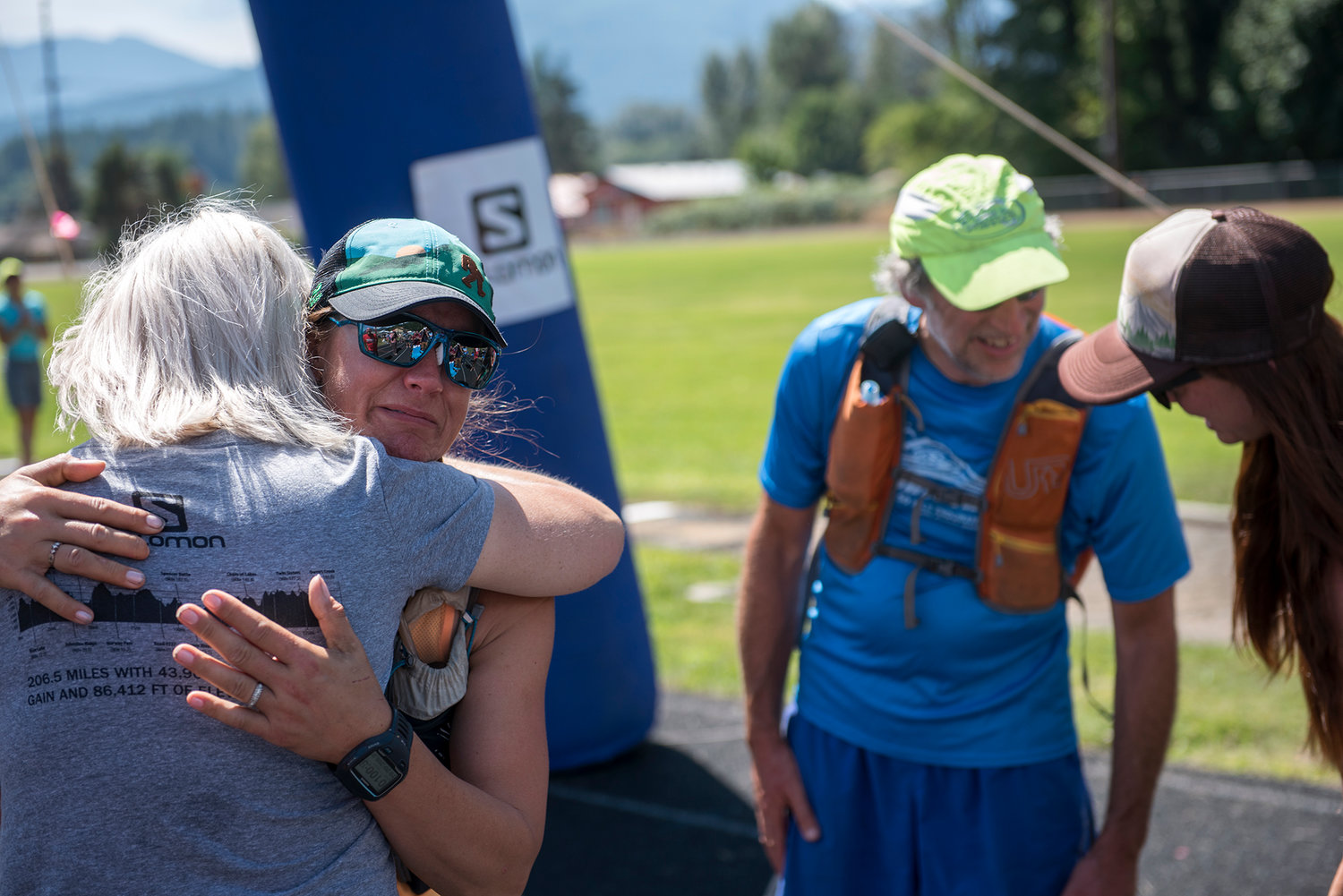 Angela Wilder of Mcleary (left with glasses) gets a hug after crossing the Bigfoot 200 finish line at White Pass High School on Tuesday afternoon. Wilder crossed the finish line with Dan Saul of Olympia (green hat) who was greeted on the track by race coordinator Candice Burt (far right).