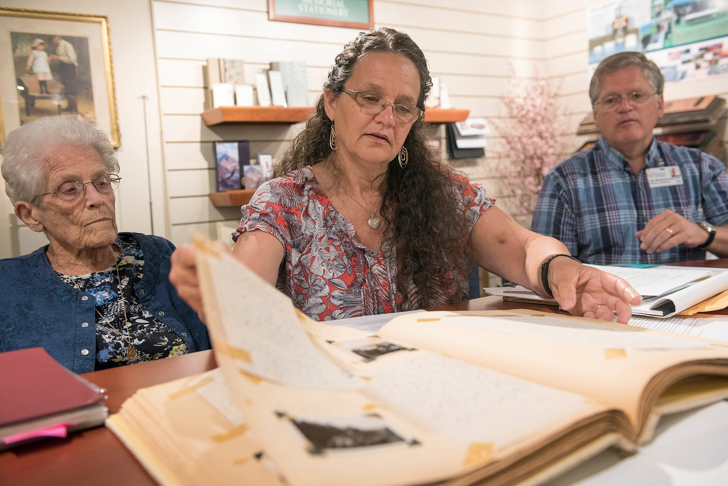 In this photo taken on Friday, July 7, 2017, Jan Bradshaw, center, alongside her mother, Jeanne Louvier, and husband, Tom, looks through a scrapbook compiled by her grandmother of her uncle's correspondences with his family while serving in Europe during World War II. William "Bill" James Gray, Jr. died while serving in Germany on April 16, 1945. 