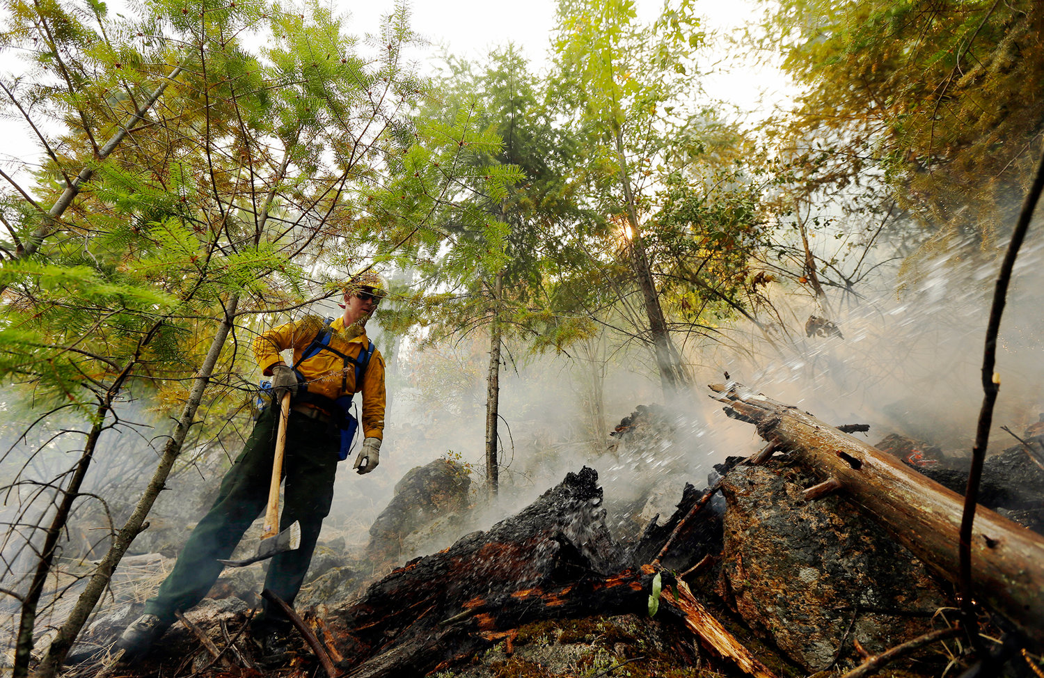 Washington National Guard Sgt. Matt Eagen, left, breaks up wood and soil looking for hot spots as the hillside is sprayed with water, Tuesday, Aug. 18, 2015, near Chelan, Wash. The troops in Washington state were part of a massive response to blazes burning uncontrolled throughout the West. (AP Photo/Ted S. Warren)