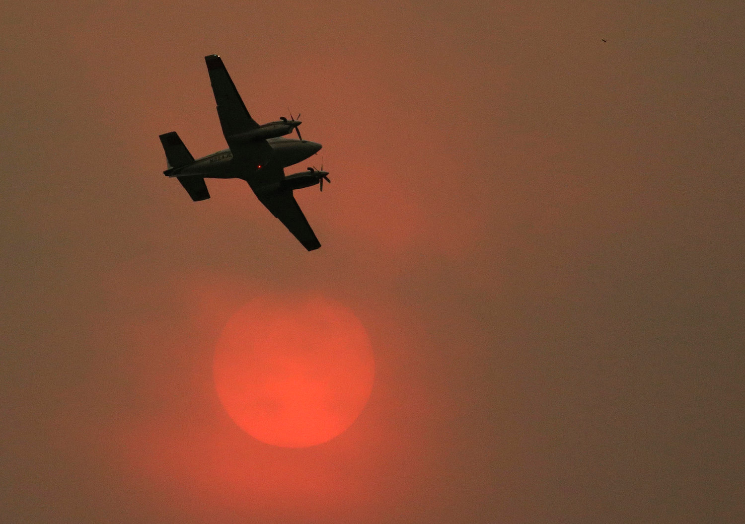 An airplane used to fight wildfires flies past the sun, which appears orange due to heavy smoke in the air while battling a blaze that flared up in the late afternoon near Omak, Wash., Thursday, Aug. 27, 2015.