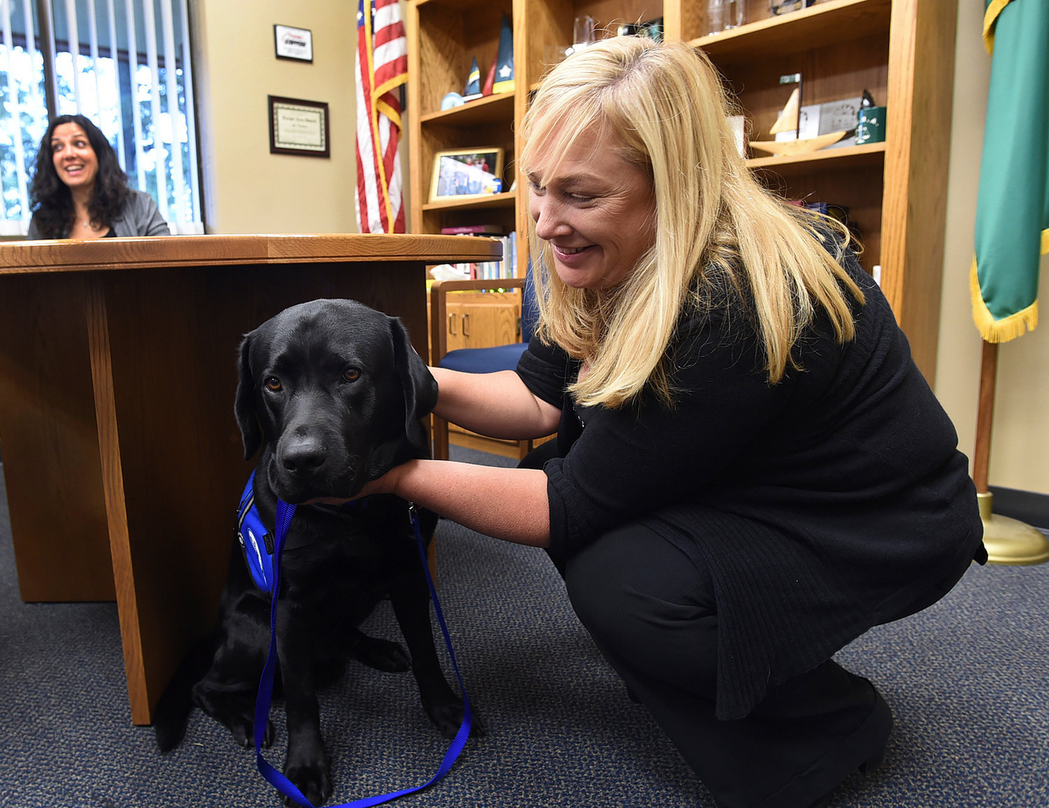 Kim Carroll, the senior victim advocate for the Thurston County Courts shows "Marshal," the new courthouse facility dog, as Wendy Ireland, the Legal Support Coordinator and caretaker of Marshal outlines the program in Olympia, Wash., Thursday, Dec. 24, 2015. The 2-year-old black lab has been specially trained to comfort crime victims at the county courthouse. (Steve Bloom/The Olympian via AP)