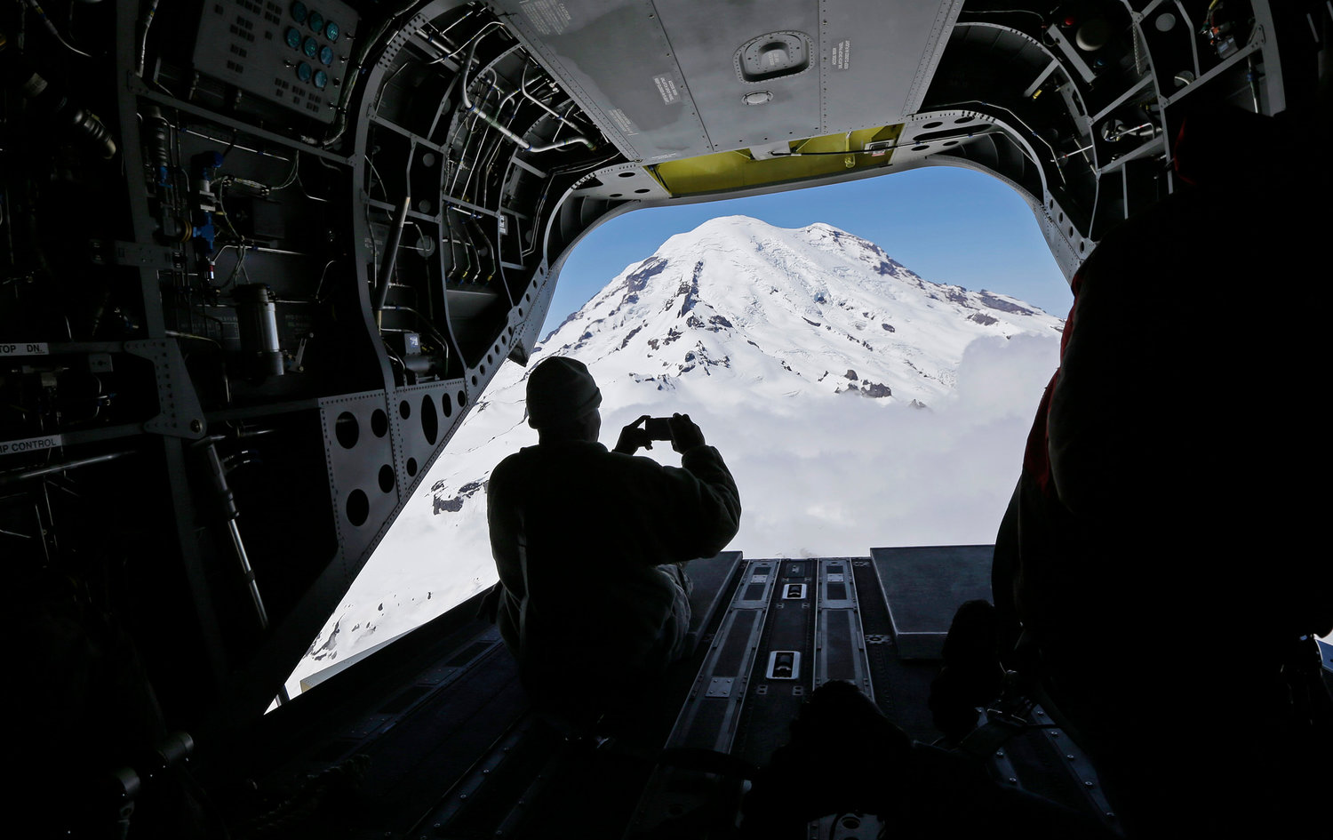 In this photo taken May 15, 2015, U.S. Army Reserve Sgt. Charlesell Thrower takes a photo of Mount Rainier out the open rear door of a Boeing CH-47F Chinook helicopter as it flies in Washington state to give members of the media a view of mountain search and rescue training exercises involving another CH-47F.