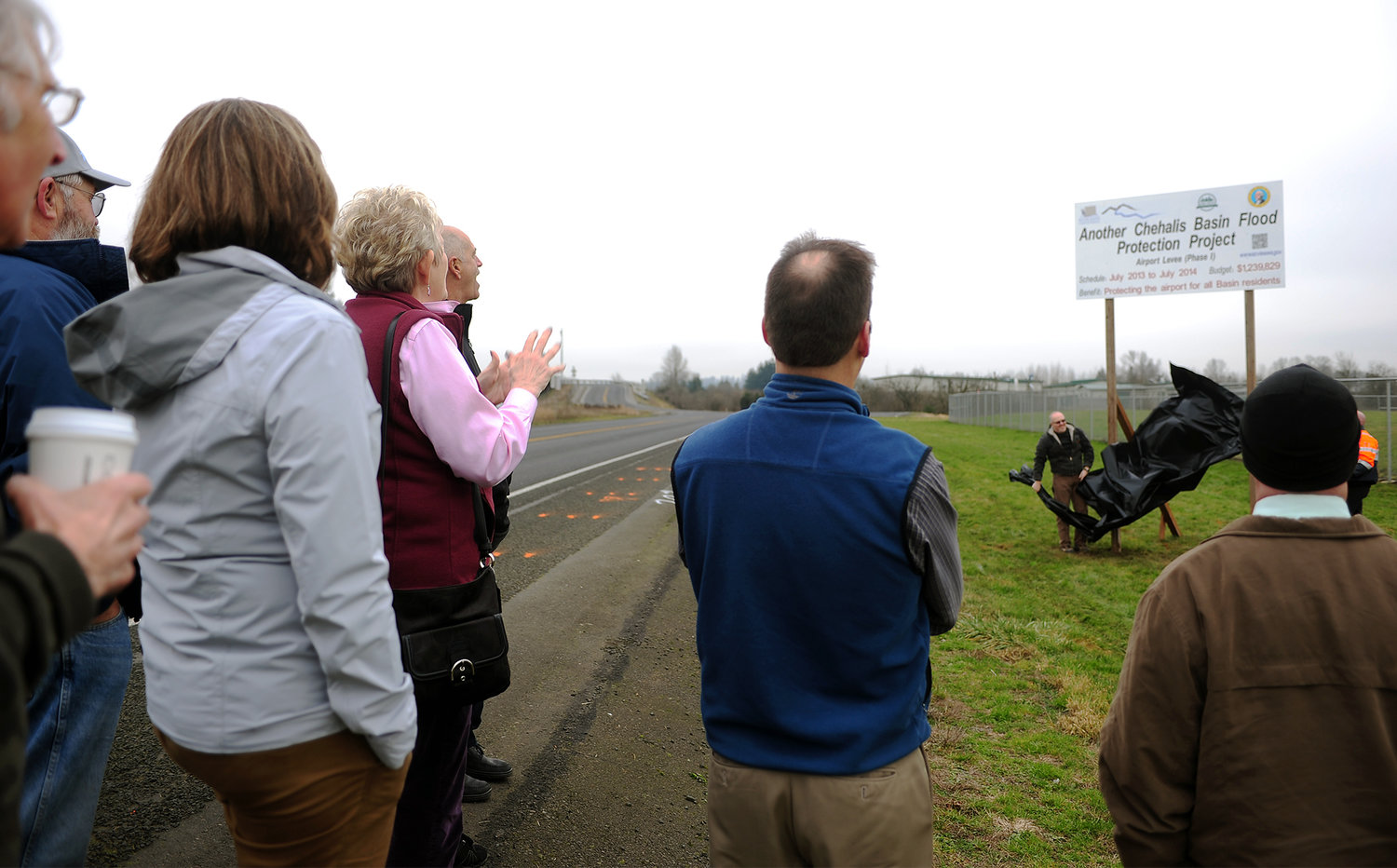 Members of the Chehalis River Basin Flood Authority work group look on as Lewis County Public Works employees unveil a new sign next to the Airport that explains where people's tax dollars are going to help flood prevention in January in Chehalis.