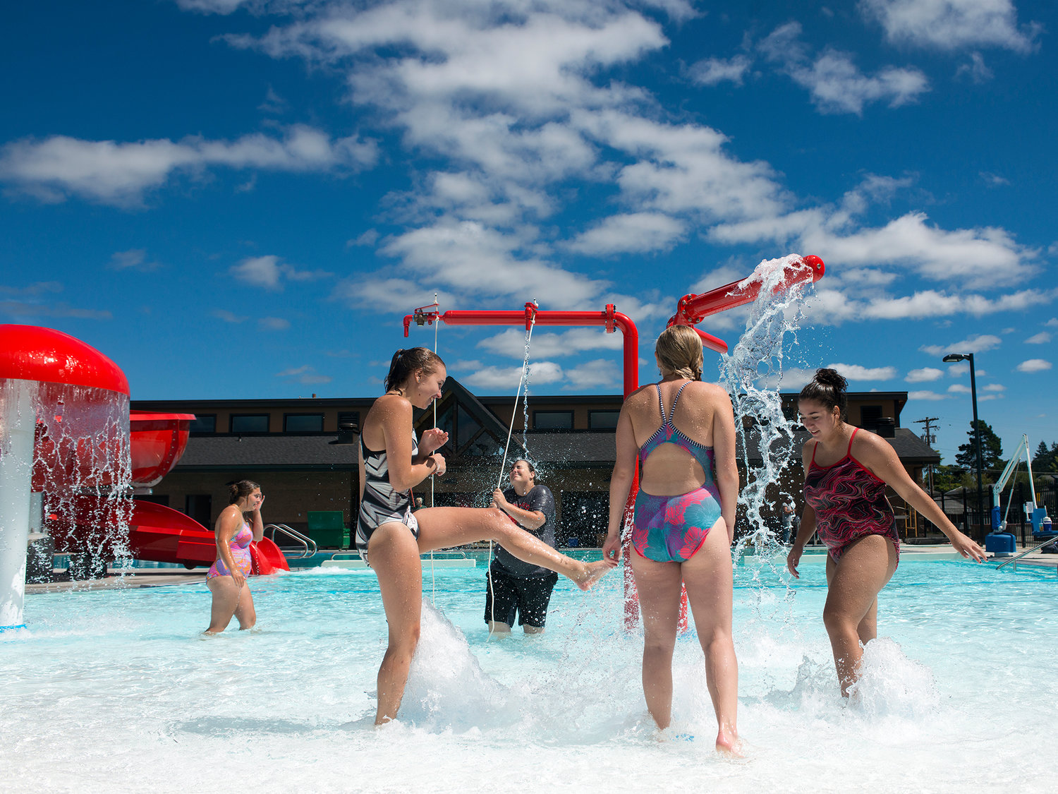 Lifeguards Hannah Cummings, left, Molly Russell, center-left, Liz Von Seggern, center, Zoe Sayler, center-right, and Raelene Heredia, right, play under one of the fountains in the zero entry area of the new Gail and Carolyn Shaw Aquatic Center in Chehalis on Tuesday afternoon.