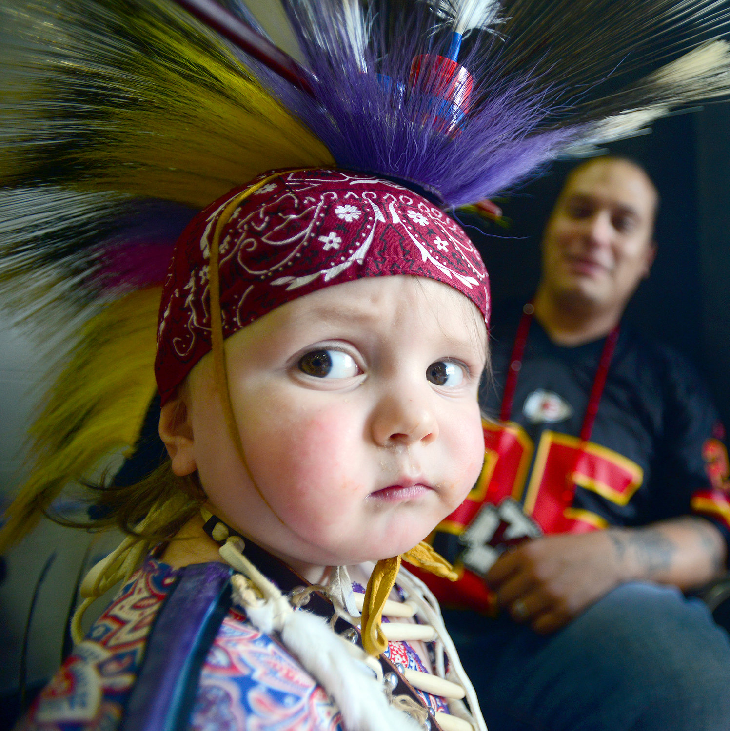 Chaytun Littleleaf, a 1 1/2 years old from Warm Springs, Ore., looks out at the dancers during a intertribal dance after his father, Owhi Littleleaf, Warm Springs, Ore., right, dressed him up for the 14th Annual Cowlitz Indian Tribe Pow-Wow at Toledo High School in Toledo, Wash., on Saturday, Sept. 21, 2013. Several hundred people attended the day-long event that featured dance contests, food vendors and raffles.