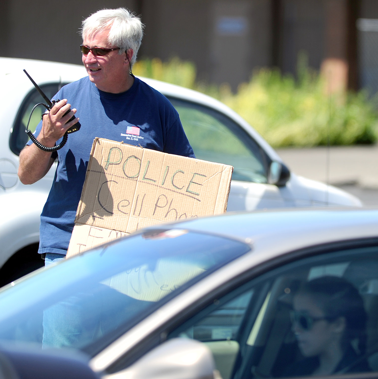 While holding a sign that reads "Police Cell Phone Emphasis in Progress," Centralia Police Sgt. Jim Shannon radios a squad car to pull over a young, female driver who was texting while stopped at an intersection at Belmont Avenue and Harrison Avenue August 2013. Gov. Jay Inslee recently signed a measure that prohibits holding an electronic device while driving, including while in traffic or waiting for a traffic light to change. 