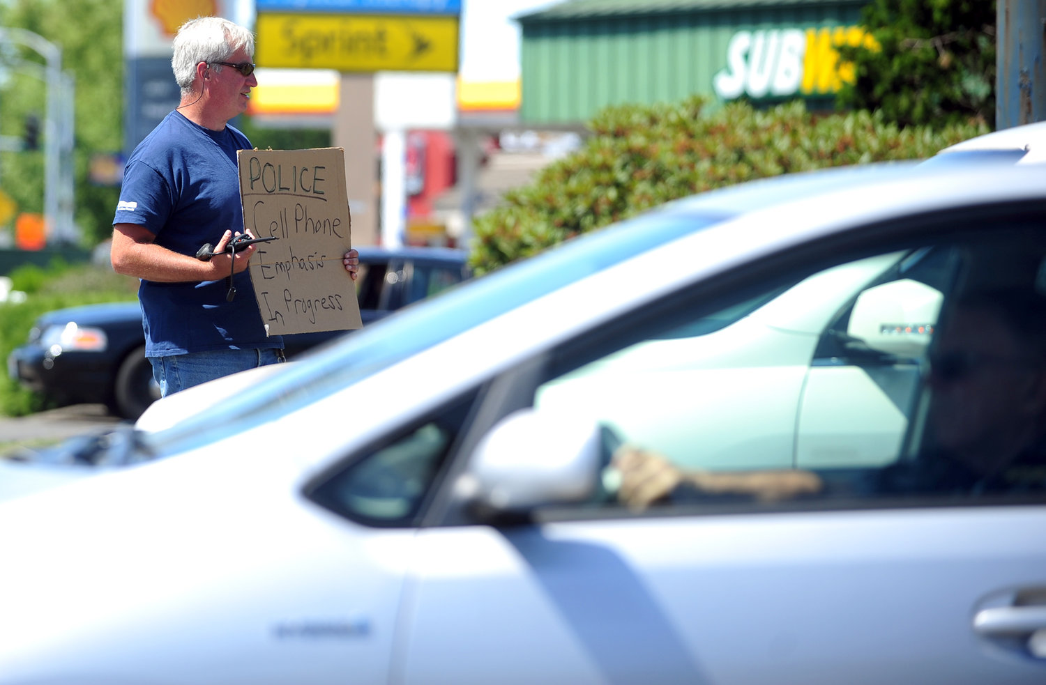 FILE PHOTO — Former Centralia Police Sgt. Jim Shannon holds a sign informing drivers of a cell phone enforcement procedure taking place near the corner of Harrison Avenue and Belmont Avenue in this August 2013 file photo.