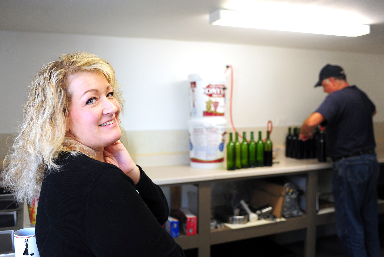 Deana Ferris looks over her shoulder as her husband, Dan, fills then corks bottles of blackberry fruit wine on Wednesday at Mill Lane Winery in Tenino.