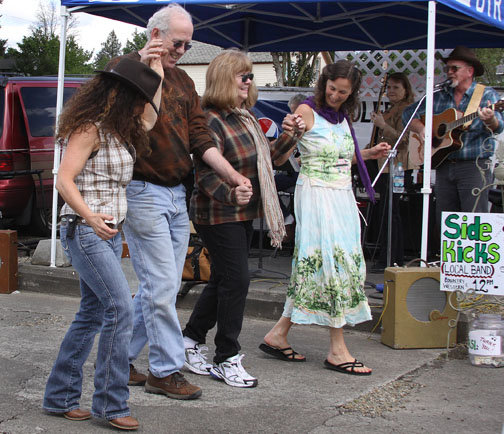 Suzanne Wiltbank, Toledo, far left, joins Alan Chappell, Toledo, second from the left, Chrisjoy Chappell, Toledo, second from the right, and Ruth Elisabeth Rose, Toledo, far right, as they line dance to the music of the Side Kicks Saturday morning at the kickoff to the new Toledo Saturday Market.