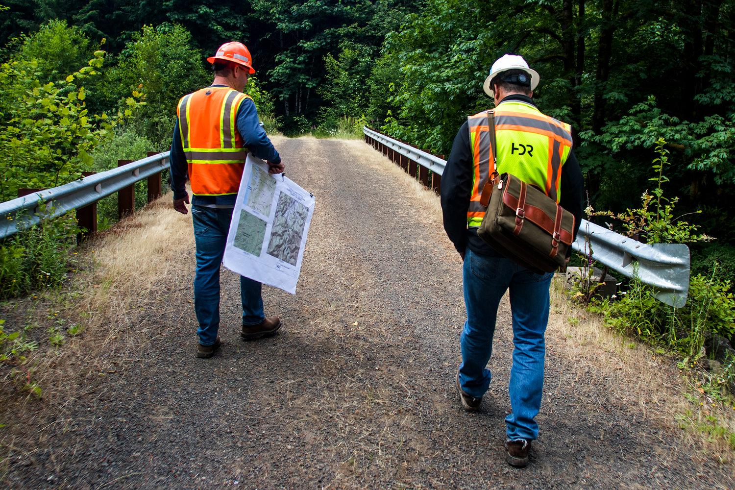 FILE PHOTO — Keith Moen, right, a project designer with HDR Engineering, and Dan Maughan, left, a member of the Chehalis Basin Flood Zone District Advisory Committee, walk on a bridge near where the dam is planned to be built in this June 2018 file photo 