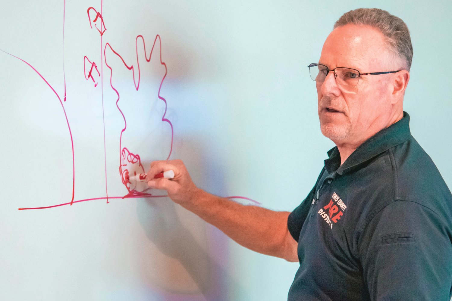 Lewis County Fire District 6 Chief Ken Cardinale draws a diagram on a whiteboard while talking about how firefighters respond to calls on Thursday.