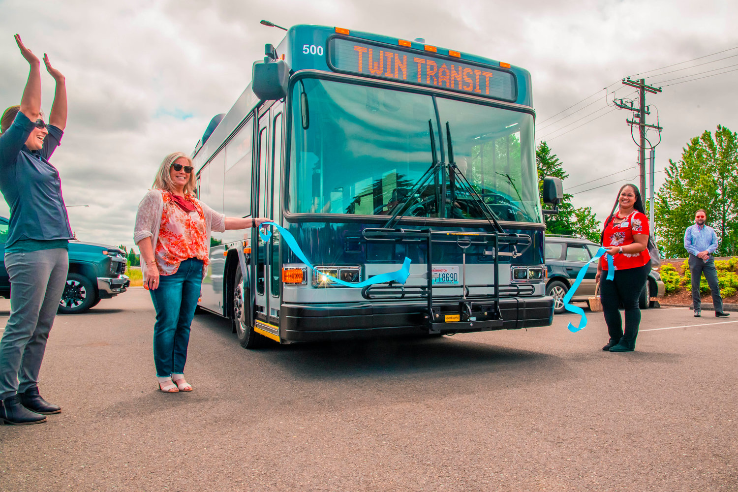 Andrea Culletto, director of Twin Transit’s community relations, raises her arms and smiles as an electric powered bus drives through a ribbon during the unveiling of the Mellen Street e-Transit Station in Centralia on Thursday.