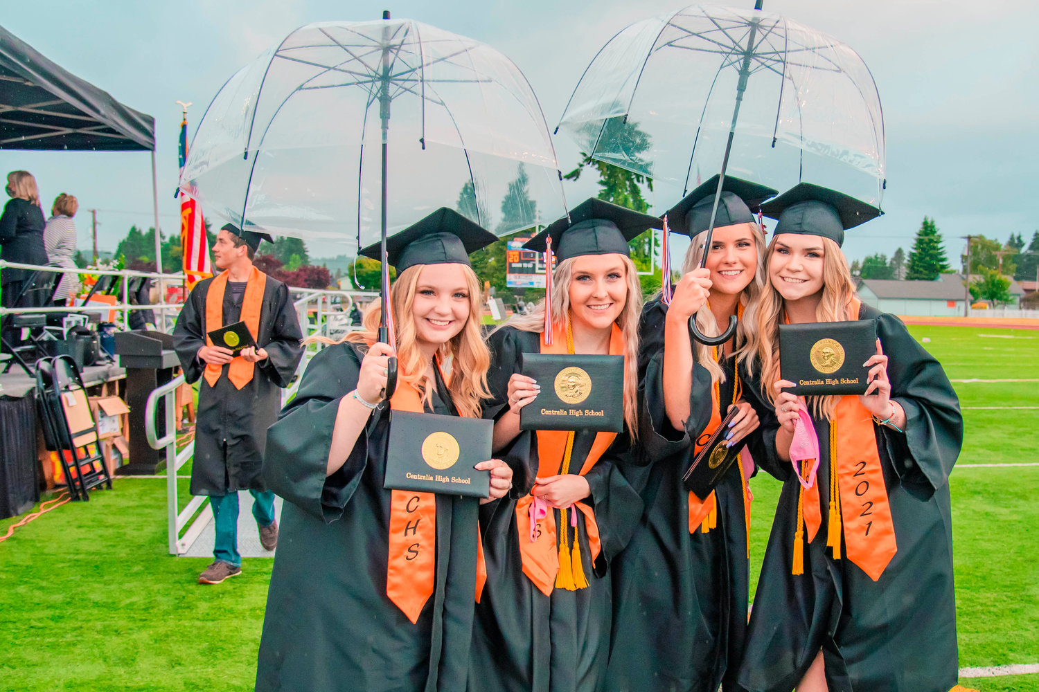 Graduates smile while holding umbrellas over their diplomas during a ceremony at Tiger Stadium in Centralia Friday night.