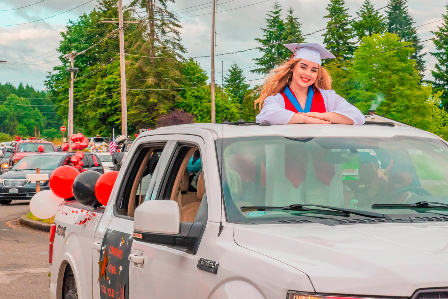 Renee Diello smiles while sporting her cap and gown and riding in the sunroof of a truck during a parade for Tenino graduates on Friday.