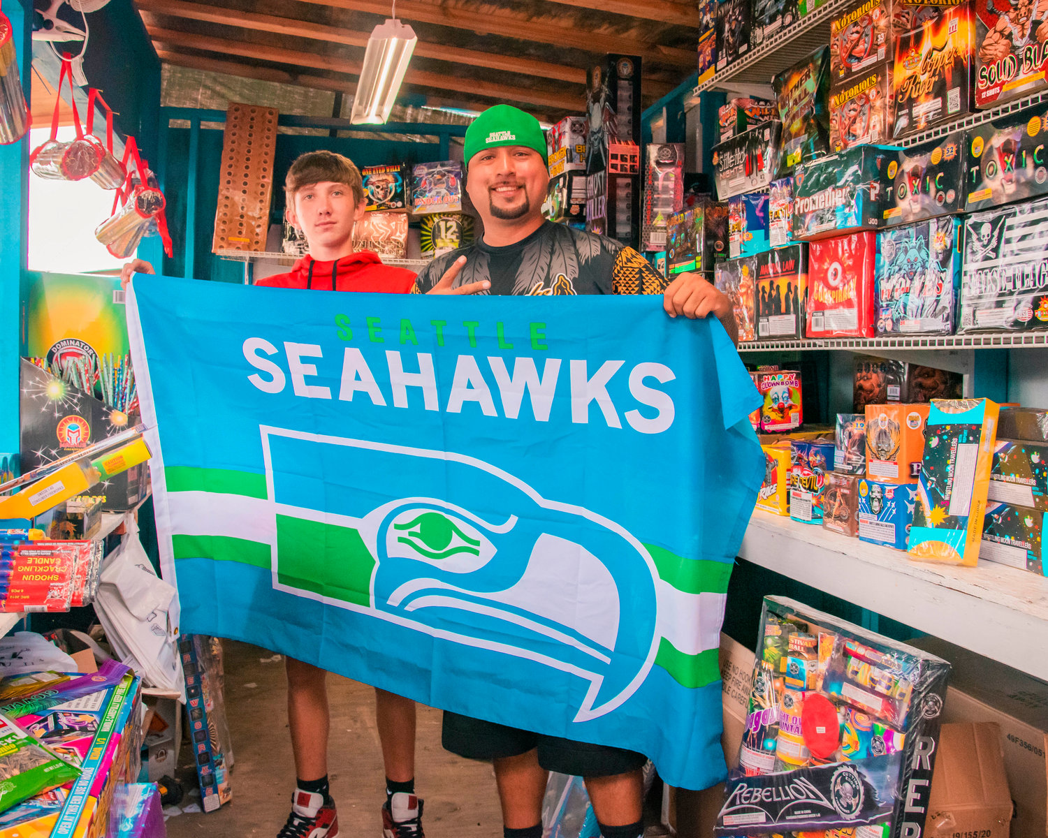 Tyler Klatush and his dad Dustin pose for a photo holding up a Seahawks flag inside their fireworks booth, which also represents their fandom, Thursday afternoon along Anderson Road SW.