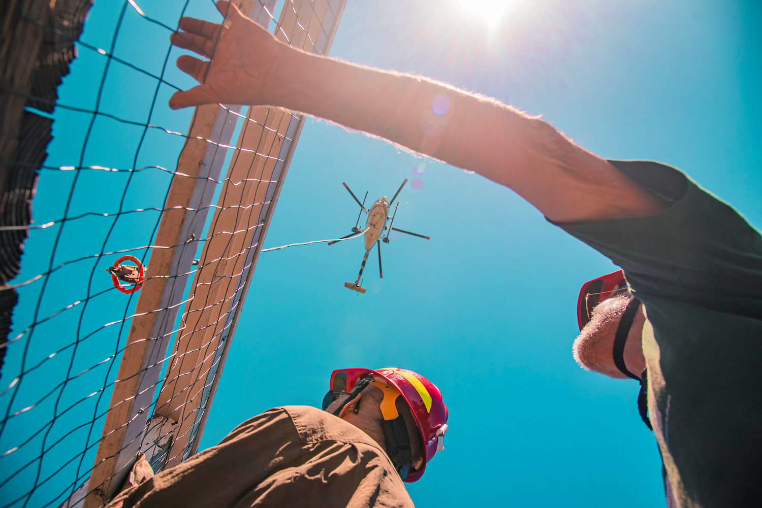A helicopter lowers a hook over High Rock Lookout as members of the Sand Mountain Society prepare to connect cargo nets full of materials to a cord during a restoration project on Tuesday in the Gifford Pinchot National Forest.