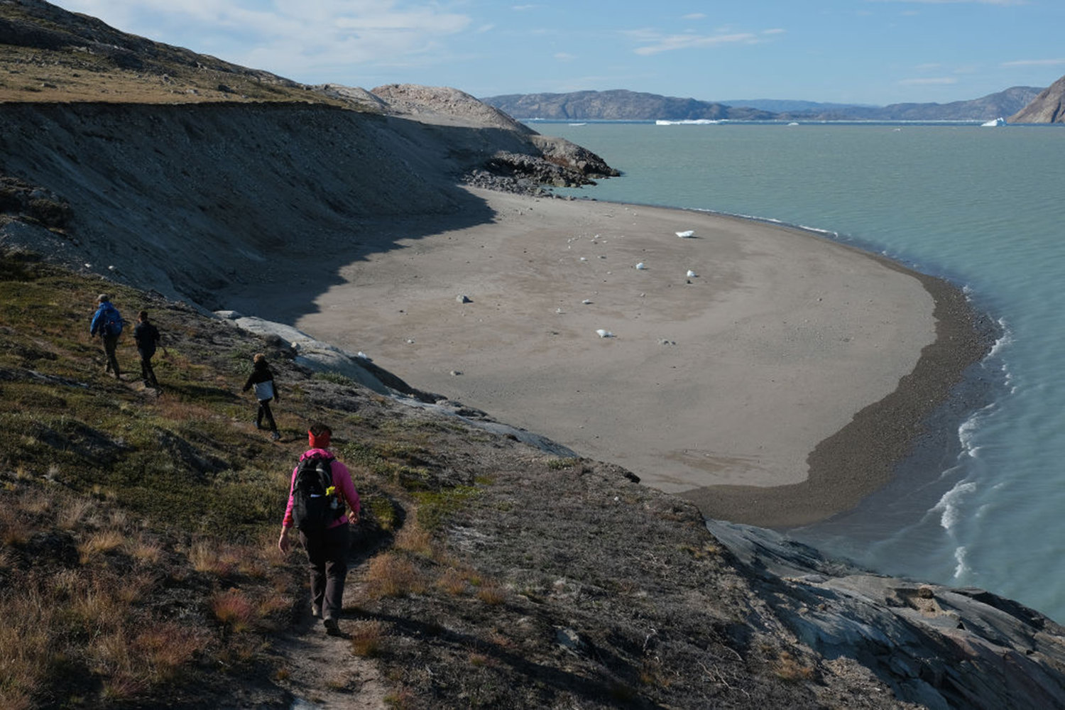 Hikers walk next to a beach shorn smooth by tsunamis resulting from ice crashing into water from the nearby Eqip Sermia glacier, also called the Eqi Glacier, on July 31, 2019 at Eqip Sermia, Greenland.
