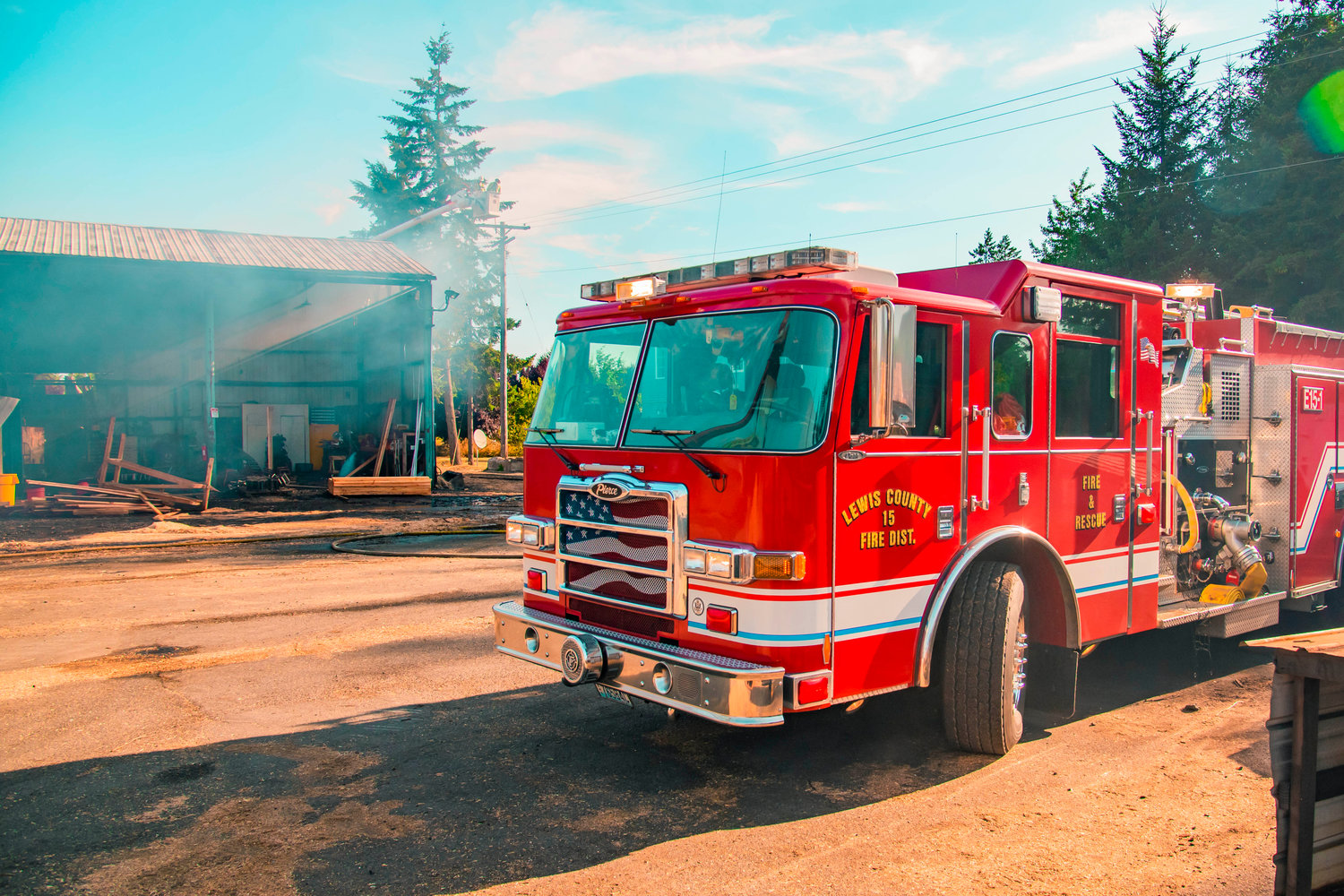 A Lewis County Fire District 15 engine is seen on the scene of a fire at Winlock Fibre as members of PUD use a bucket truck to work on utility lines near a damaged structure early Wednesday morning.
