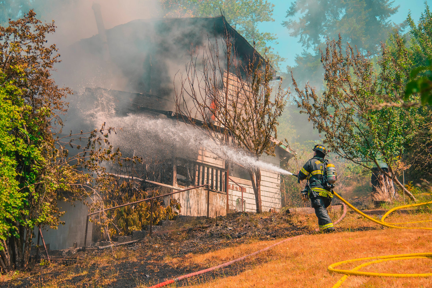 A Riverside Fire Authority firefighter uses a hose to put out flames at a residential structure on East Third Street in Centralia on Thursday.