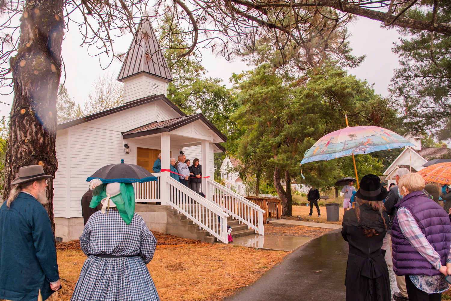 Attendees gather, some sporting vintage attire and umbrellas, during a ribbon cutting ceremony for the Borst Park Pioneer Church in Centralia on Saturday.