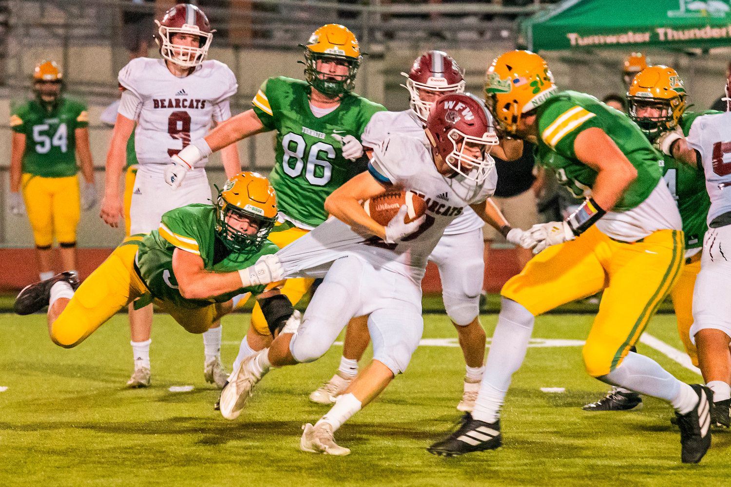 W.F. West’s Jacob Fuller (2) continues to pick up yardage as Tumwater’s Caleb Sadlemeyer (55) hangs off his jersey during a game Friday night.