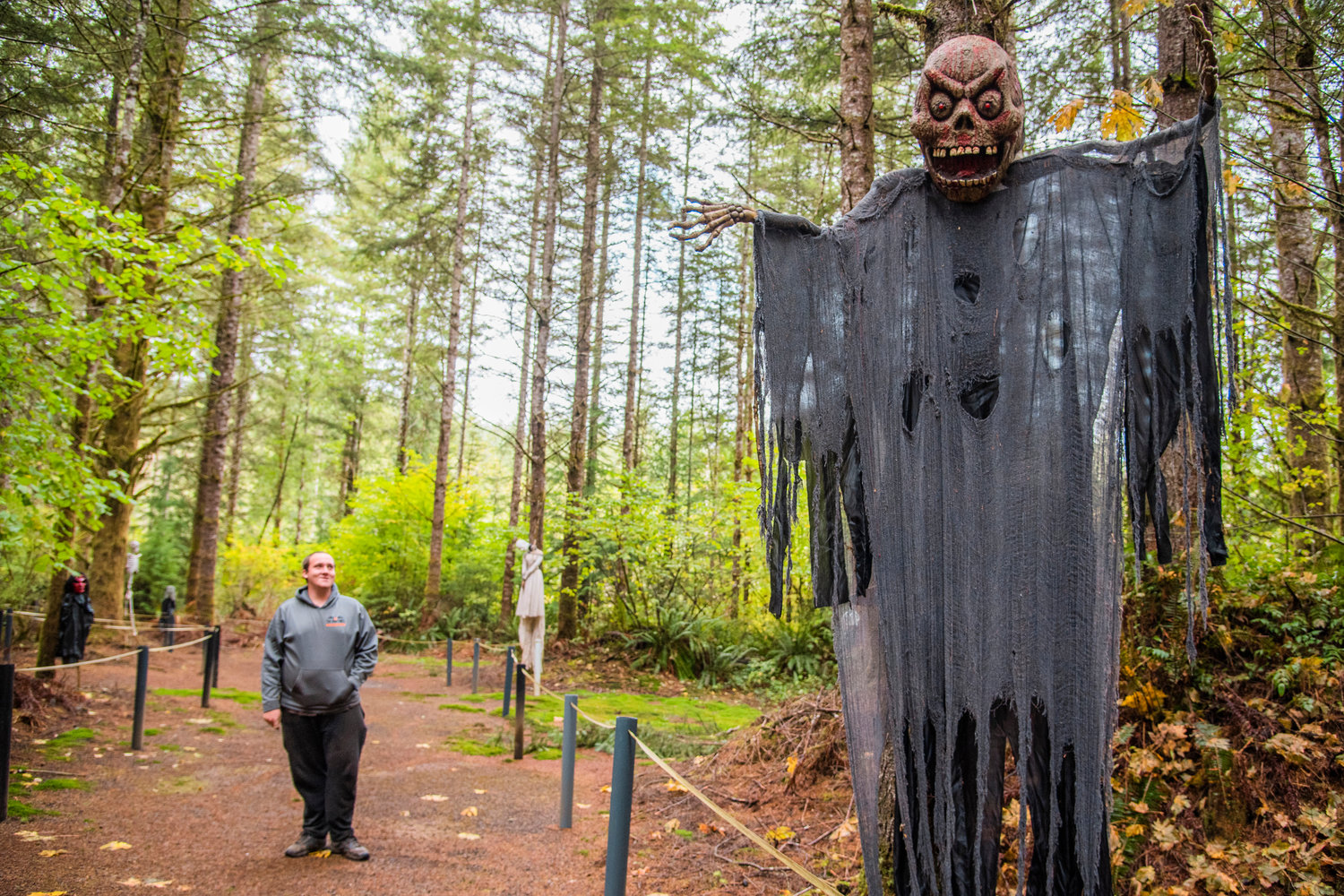 Landon Huntting smiles and looks up to a large spooky figure hung on a tree inside the haunted forest at The Huntting’s Farm in Cinebar.