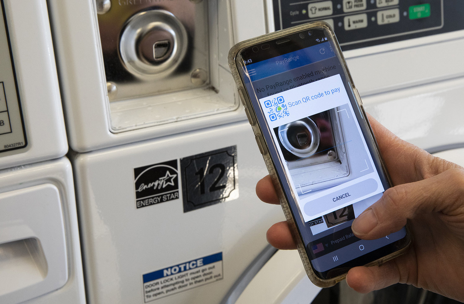 Heidi Thorsen, owner of Lunar Laundry in Seattle’s Ballard neighborhood, holds her phone near one of her washing machines on Wednesday, Nov. 17, 2021, near where a QR code will soon be placed.  In approximately two weeks, customers will be able to use a PayRange app to pay to operate the machines. Thorsen is dealing with a shortage of quarters at her Ballard laundromat. (Ellen M. Banner/Seattle Times/TNS)