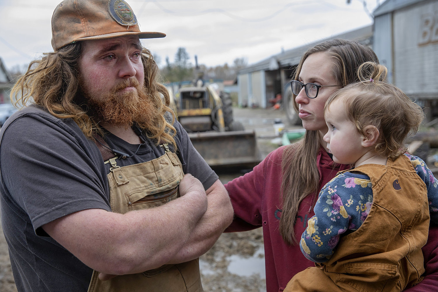 Jordan Baumgardner, left, is consoled by his wife, Jamie, who holds their daughter, Grace, on Nov. 24, 2021, in Mount Vernon, Washington, at the family dairy farm that lost cows in flooding. Jordan, the farm's herdsman, struggled in flood waters in the night to save 250 dairy cows and is still reeling from losing 44 of them.  (Ken Lambert/Seattle Times/TNS)