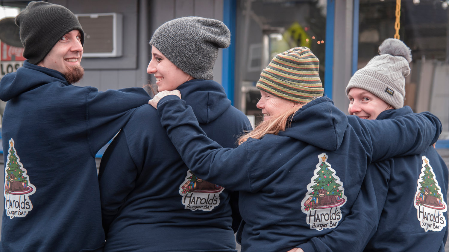 Harold’s Burger Bar staff smile and and embrace while showing off custom hoodies with Christmas themed logos in Centralia.