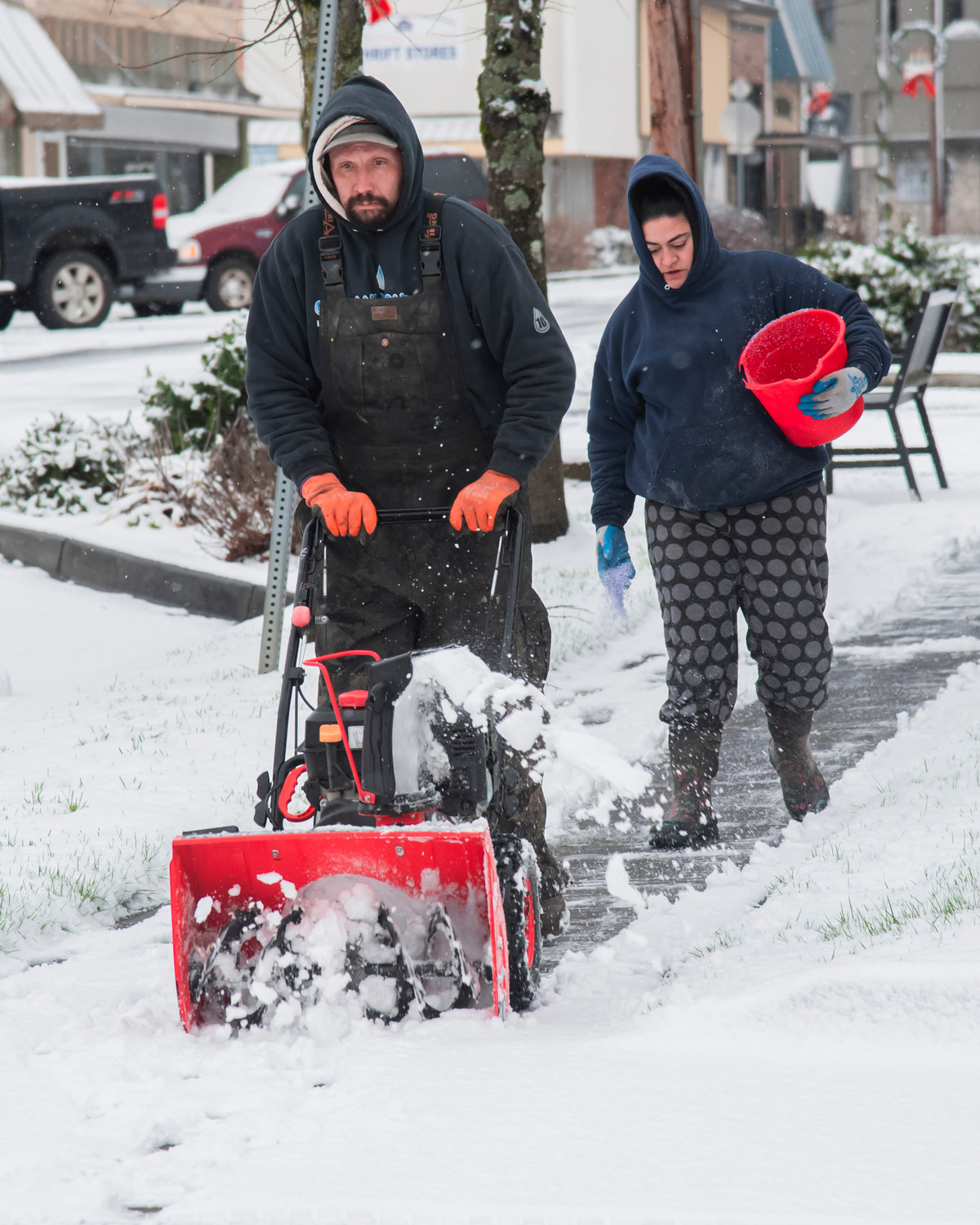 KW Weaver clears sidewalks in Chehalis as Angie Schlueter pours salt along the walkway Sunday morning.