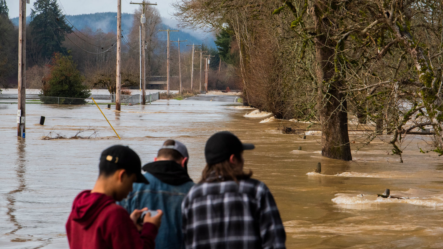 Locals walk down to the waters edge and look on as the Chehalis River overflows into Scatter Creek inundating Independence Road SW, and nearby properties in Rochester on Saturday.