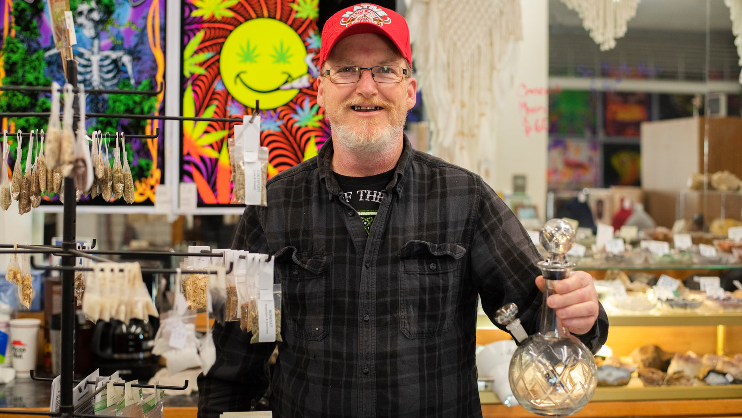 Paul Bromm smiles while holding a custom glass piece inside his shop StrangeLands in downtown Centralia.