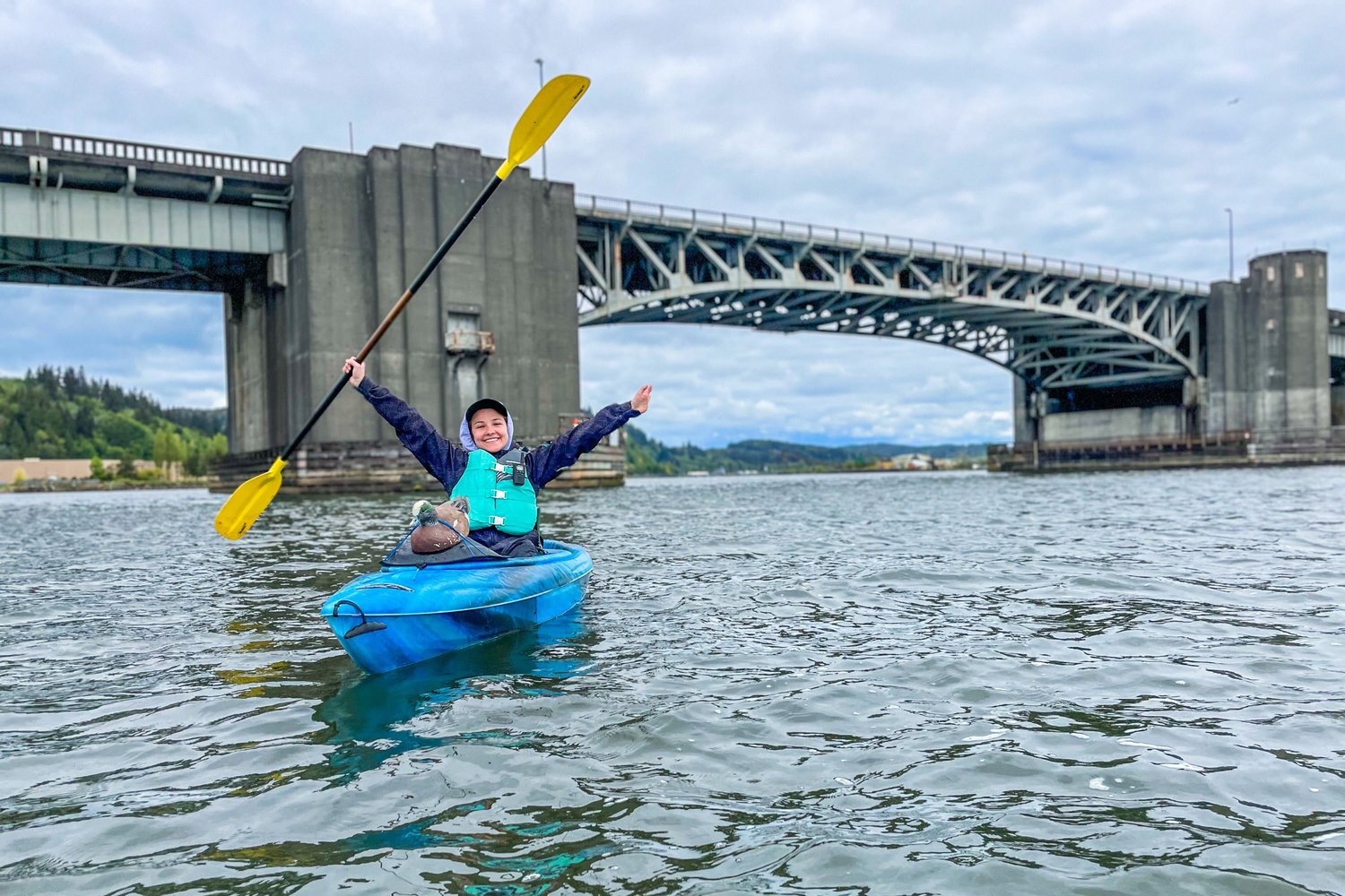 Reporter Isabel Vander Stoep holds up her paddle and smiles after paddling under the Chehalis River Bridge in Aberdeen.