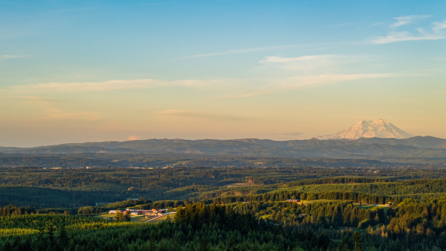 The sky glows a hazy peach color over Mount Rainier and the Twin Cities as the sun begins to set on the summer solstice, seen from Crego Hill in Adna.