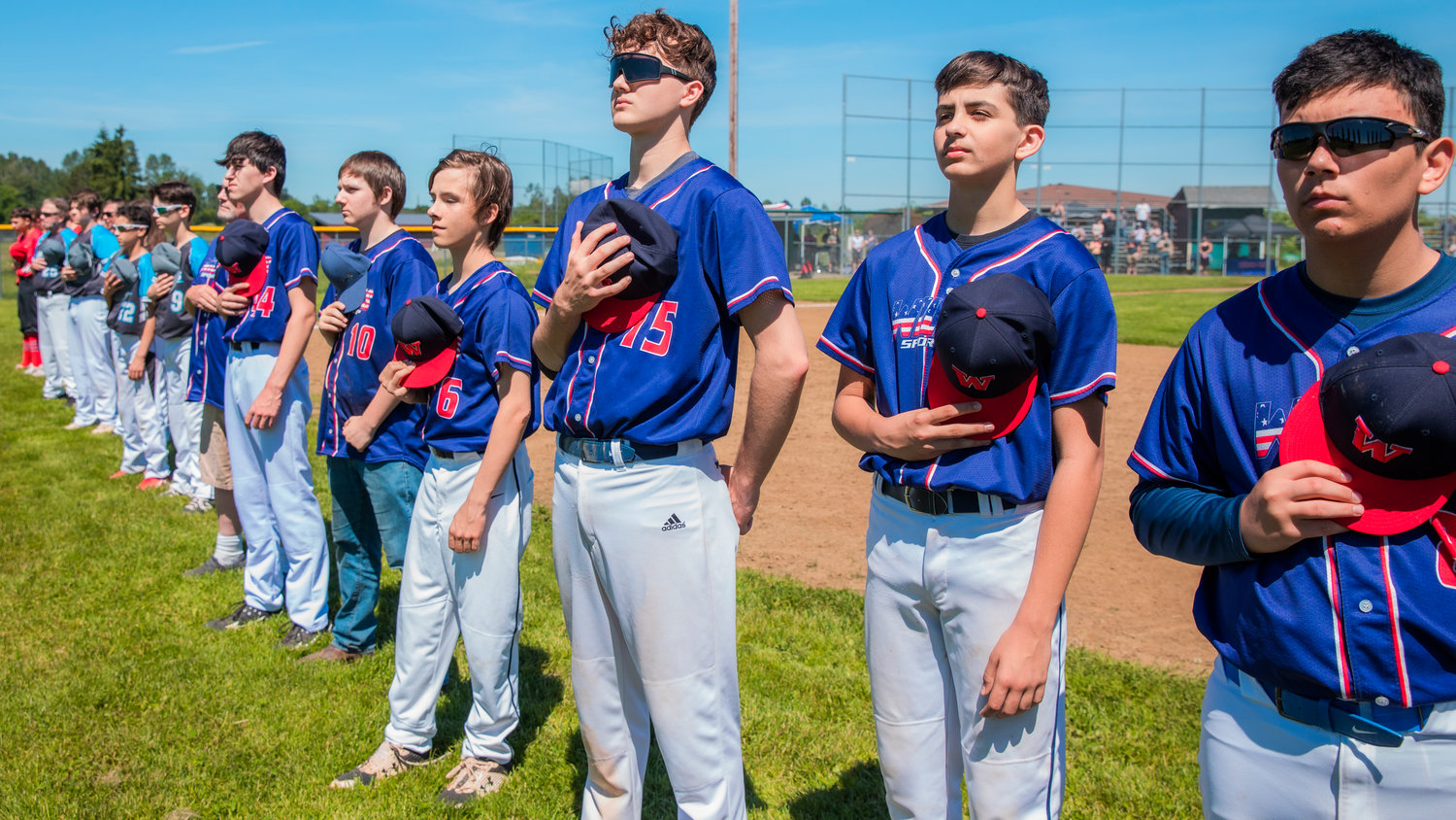 Players use caps to cover hearts as the national anthem plays at Stan Hedwall Park in Chehalis on Saturday for closing ceremonies.
