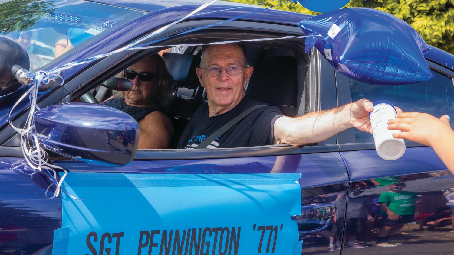 Former Toledo Police Department sergeant Randy Pennington, who retired July 5 after 36 years, smiles and passes out water bottles while driving through downtown Toledo during the Cheese Days parade in a cruiser decorated with balloons last weekend.