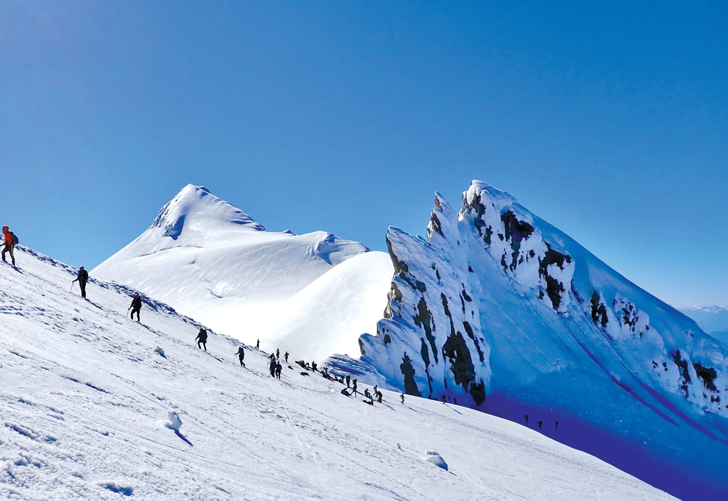 Climbers walk with poles along the snowy slopes of Mount Baker.