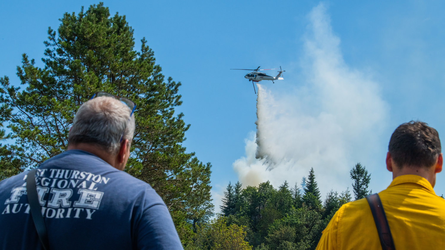 West Thurston Fire Authority Chief Robert Scott watches alongside crews from the Department of Natural Resources as a helicopter flies overhead dumping water on a forest fire near Bucoda after pulling water from the Skookumchuck River Monday afternoon.