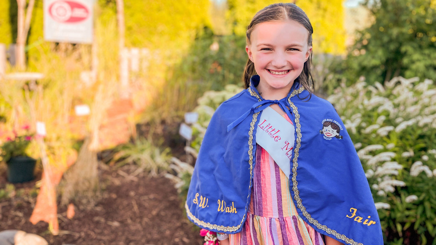Little Miss Friendly Emma Britton, sporting the iconic cape, smiles for a photo Tuesday at the Southwest Washington Fairgrounds in Centralia.