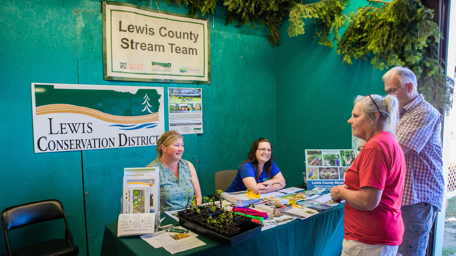 Nikki Atkins, watershed liaison, and Kelly Verd, special projects coordinator for the Conservation District, smile and talk to visitors at their table inside the Wildlife Building at the Southwest Washington Fairgrounds in Centralia on Tuesday.