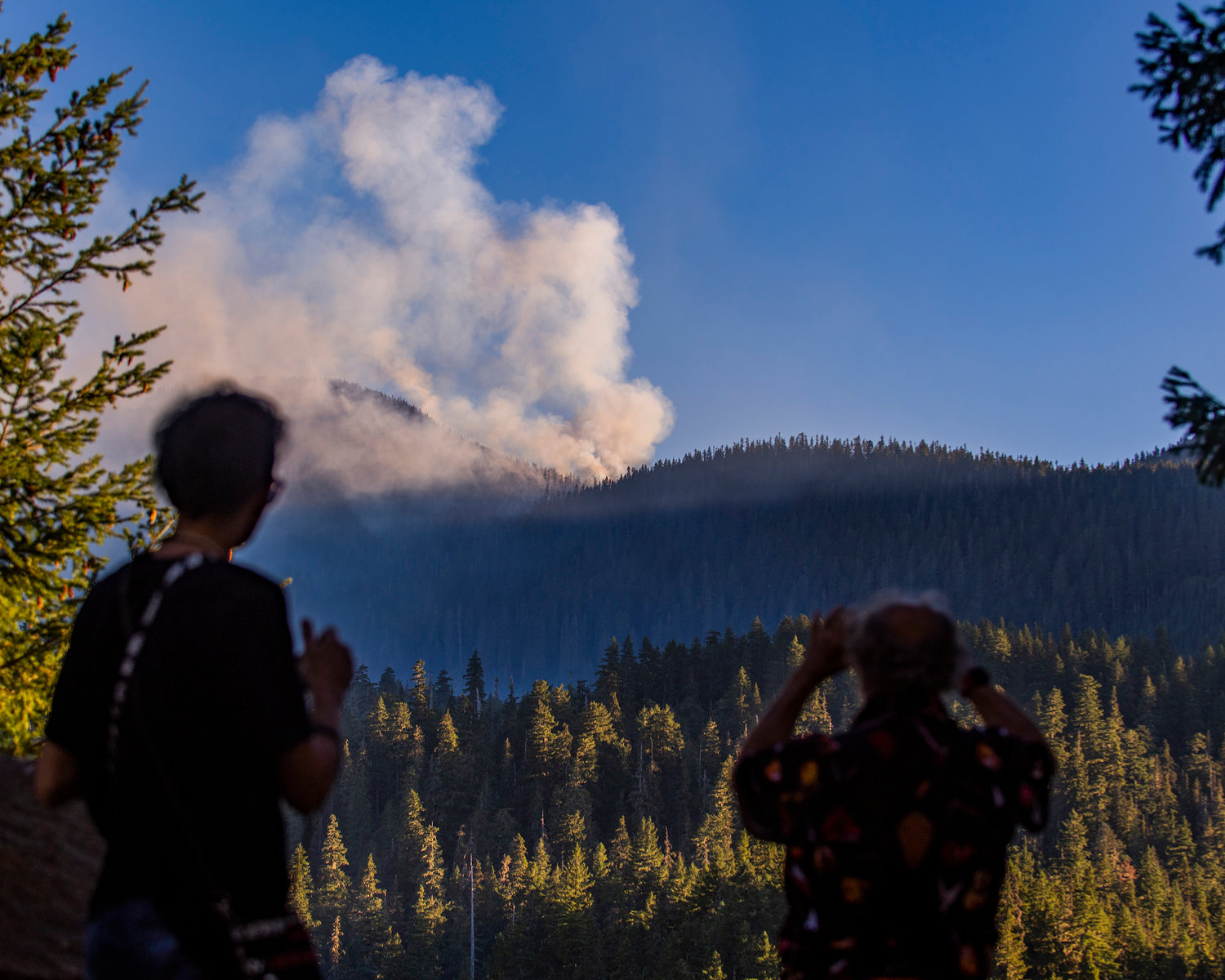 Tom Pell, of the Tri-Cities, right, stops along U.S. Highway 12 east of Packwood to photograph the Goat Rocks Fire with his cellphone on Tuesday.